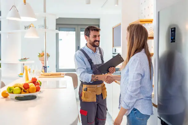 Home service professional shaking hands with a satisfied customer in a modern kitchen, showcasing reliable and friendly home repair services.