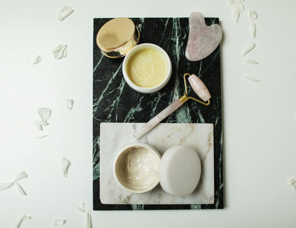 Luxury skincare setup with massage oil, jade roller, and gua sha stone on marble tray, promoting at-home relaxation massage routine.