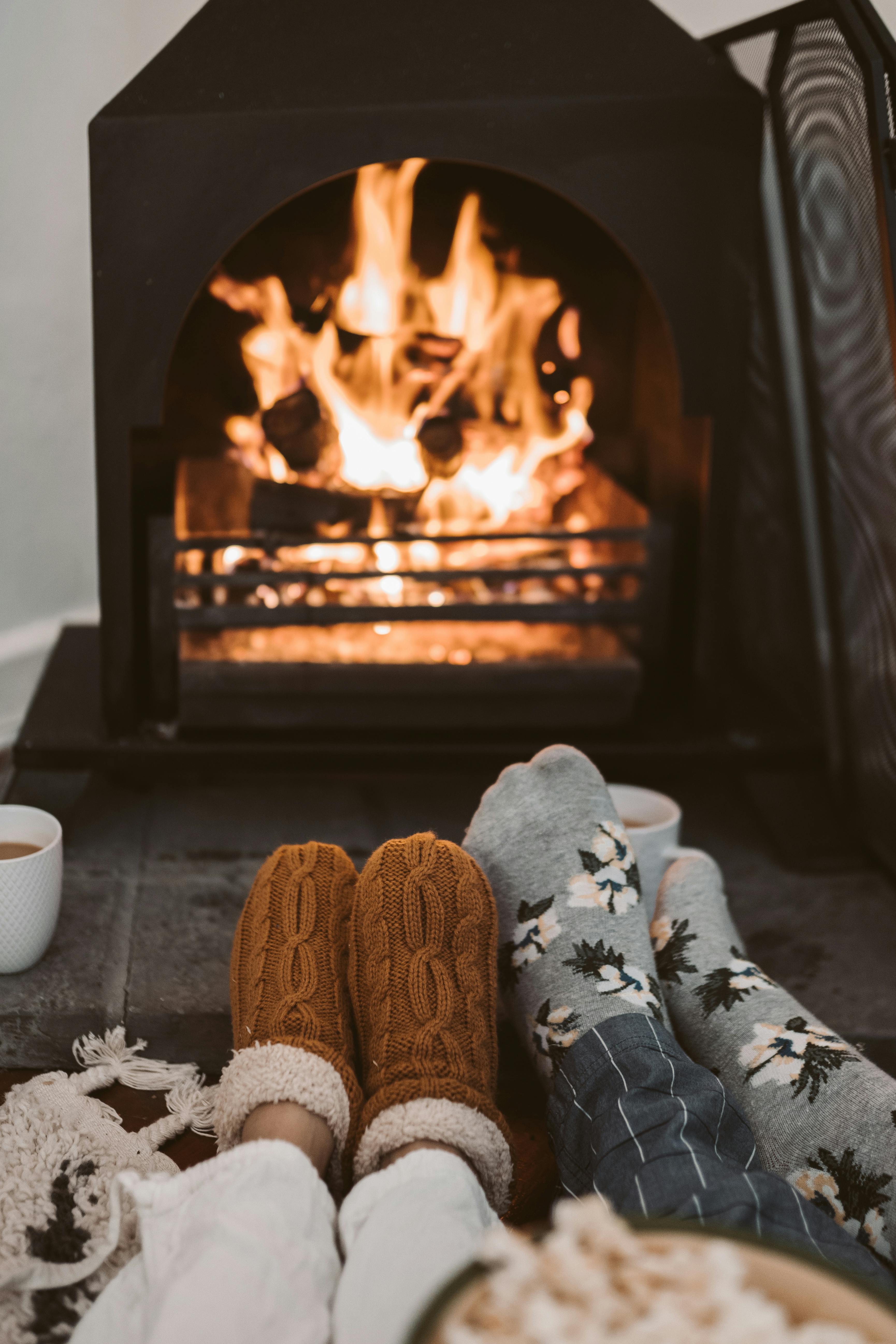 Cozy winter scene with two people warming their feet by a roaring fireplace, enjoying hot drinks. Winter home comfort in Amsterdam.